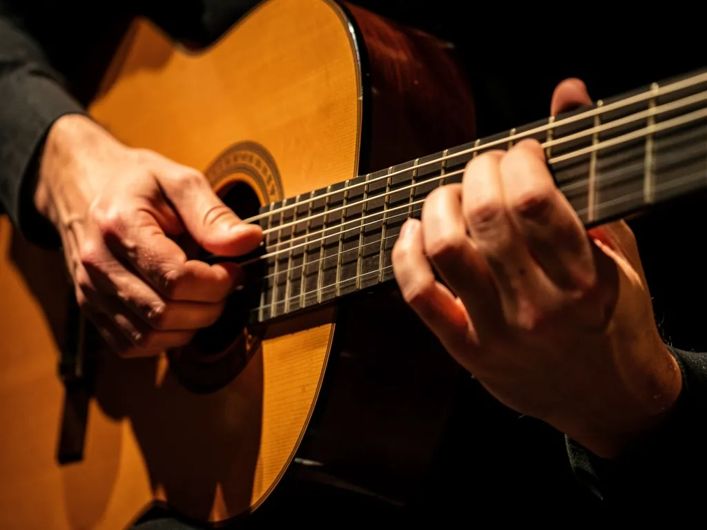 Mãos de violonista pressionando acorde complexo no braço do violão com iluminação dramática de palco